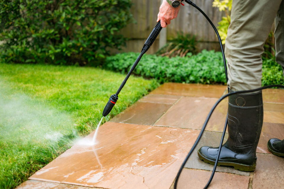 man using high pressure washer to clean stone patio