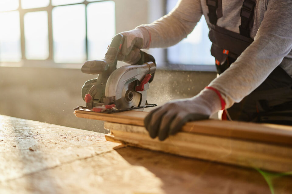 man using small electric saw to cut wood plank